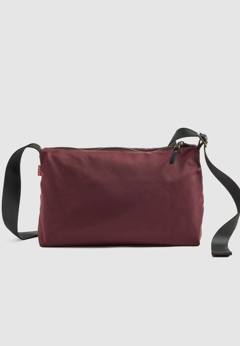 Bordeaux rektangulær crossbody-tasker med sort justerbar rem og lynlåslukning foroven mod en ensfarvet baggrund.