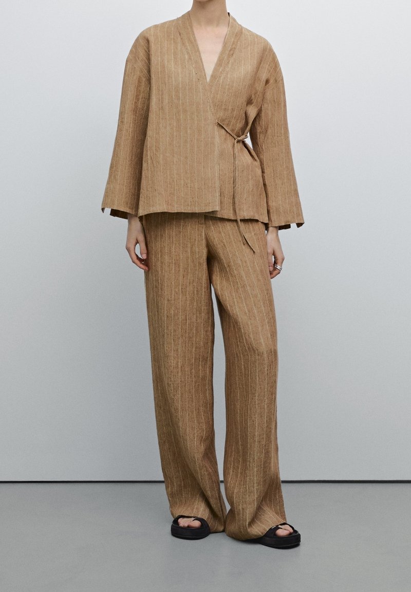 Ensemble deux pièces rayé marron fait d'un tissu texturé ; il comprend un haut croisé avec de larges manches et un pantalon ample.