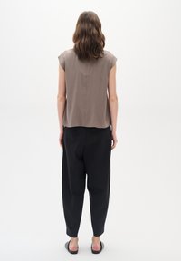 Maglietta marrone a maniche corte con vestibilità rilassata, abbinata a pantaloni neri a sigaretta. Texture morbide con dettagli di design minimalisti.