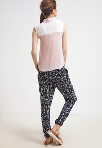 Light pink sleeveless blouse with a white collar, paired with black patterned joggers featuring green and pink foliage designs, and light footwear.
