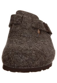Zoccolo in felt marrone con punta arrotondata, fascia regolabile e superficie strutturata. Presenta una suola in gomma per aderenza e durata.