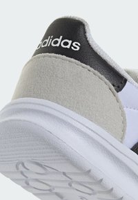 Päta tenisky Adidas so zvrškom z čiernej kože, stredom z šedej semišovej látky a bielou gumovou podrážkou s textúrovanými vzormi pre lepšiu priľnavosť.