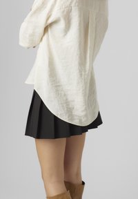 Beige linne skjorta med rundad nederkant, ihop med en svart veckad kjol. Outfiten inkluderar bruna ankelstövlar. Mjuk textur, avslappnad passform.