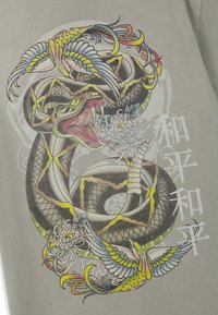 Aufgerollte Schlange mit offenem Maul, umgeben von zwei bunten Vögeln und weißen Blumen, überlagert von weißen japanischen Schriftzeichen auf grauem Hintergrund.