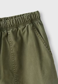 Olive green pants with elastic waistband and side seam pockets, shown against a plain light gray background.