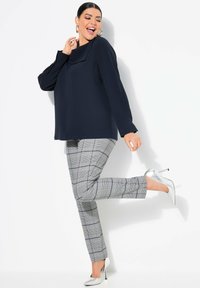 Marineblouse met gedrapeerde halslijn, gecombineerd met grijs geruite skinny broek en zilveren hoge hakken. Gladde stof en op maat gemaakte silhoette.