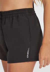 Crne kupaćice izrađene od laganog materijala, s elastičnim pojasom i bijelim "O'NEILL" logotipom sa strane.