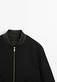 Veste bomber noire avec col en maille côtelée et fermeture éclair argentée, présentée sur fond blanc.