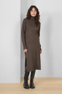 Robe pull marron à manches longues et fentes sur les côtés, faite en tissu texturé. Portée avec des bottes en cuir noires arrivant aux genoux.