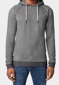 Grijze hoodie met een textuurpatroon, witte koordjes en een donkere ribbelrand. Lange mouwen en een ontspannen pasvorm, gecombineerd met denim jeans.