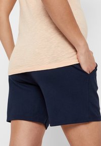 Navy blue cotton shorts with side pockets, featuring a smooth texture and a fitted design, paired with a light peach top.