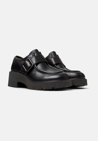 Chaussures en cuir noir avec un bout rond, détail de boucle sur le côté et semelle épaisse texturée. Design élégant et moderne avec une finition mate.