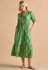 Zielona sukienka maxi w kwiatowy wzór z krótkimi bufkami, elastycznym pasem i warstwowym dołem. Lekki materiał o teksturowanym wyglądzie.
