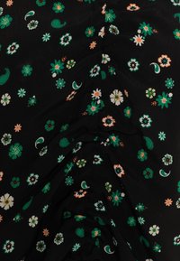Tessuto nero con piccoli motivi floreali e paisley verdi, bianchi e arancioni, leggermente arricciato o drappeggiato al centro.
