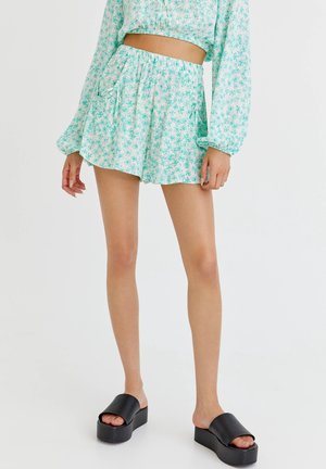 Shorts floraux bleu clair avec une taille élastique et un cordon de serrage ; associés à des sandales à plateforme noires ; tissu lisse.