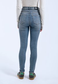 Jeans de tiro alto, ajustados, en denim azul claro con una textura suave, que cuentan con bolsillos traseros y una etiqueta de marca negra en la cintura.