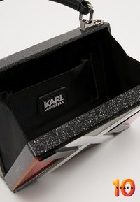 Czarna torebka o strukturalnym kształcie z błyszczącą srebrną ramą, wewnątrz materiałowa podszewka i metka z logo KARL LAGERFELD. Zapięcie magnetyczne.