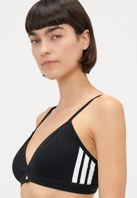 Crna trokutasta bralette s tankim trakama, s bijelim vertikalnim trakama sa strane, izrađena od glatkog materijala.