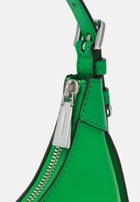 Grøn lædertaske med en triangular form, sølv lynlås hardware og kontrasterende sort trim. Har en glat tekstur og synlige syningsdetaljer.