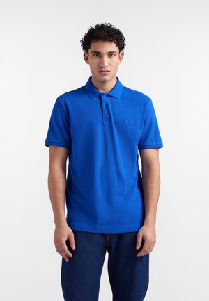 Niebieska koszulka polo z bawełny, z klasycznym kołnierzykiem, krótkimi rękawami oraz małym haftowanym logo na lewej piersi. Noszona z ciemnymi dżinsami.