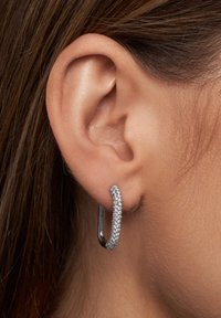 Silverörhänge med en böjd design och en rad små, glittrande ädelstenar längs ena kanten, hängande från örsnibben.