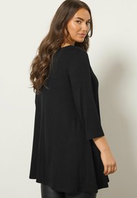 Tunica nera con maniche a tre quarti, caratterizzata da una silhouette a linea A e tessuto morbido. Texture liscia, dettagli minimi e design classico.
