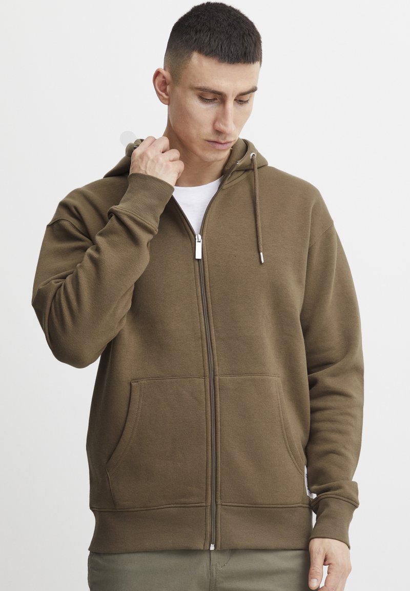 Brun zip-up hettegenser laget av mykt materiale med lommer foran, ribbede mansjetter og justerbar hette. Glatt tekstur med en avslappet passform.