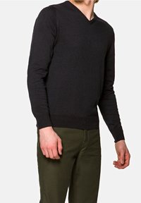 Suéter negro de cuello en V en una tela suave de punto; diseño ajustado con mangas largas; combinado con pantalones verde oliva; detalles mínimos.
