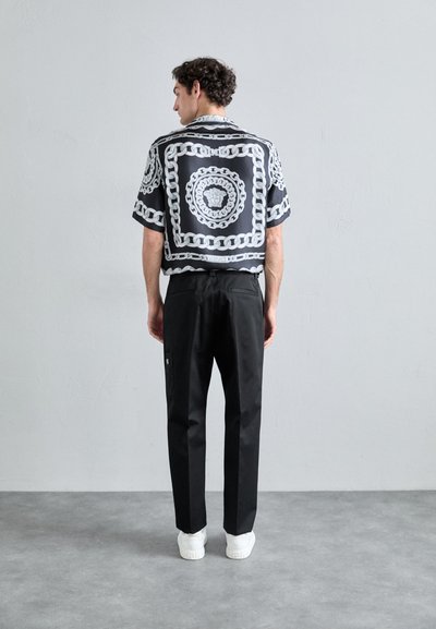 Short-sleeve black shirt with white chain print, paired with black pants and white sneakers. Visible tag on pants, plain background.