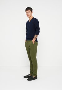 Sweater azul em V, calças verdes ajustadas e sapatos pretos de slip-on. Textura de malha suave, design casual, ajuste moderno e cores contrastantes.