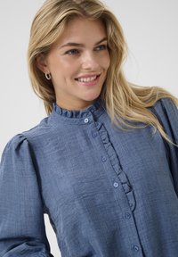 Helles blaues Bluse aus strukturiertem Stoff, mit Rüschekragen, Knopfleiste und puffigen langen Ärmeln.