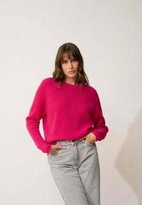 Felle roze trui gemaakt van textuur gebreide stof, met een ronde hals en lange mouwen, gecombineerd met hooggesneden grijze jeans.