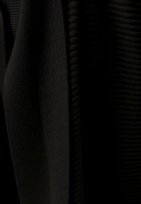 Musta kangas, jossa on ribboitettu rakenne ja sileät alueet, jotka korostavat vaihtelevaa syvyyttä ja hienovaraista kiiltoa pinnalla.