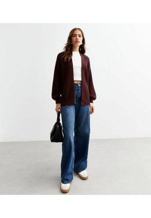 Maroon knitted cardigan with wide sleeves, white crop top, and blue wide-leg jeans. White shoes with tan soles and a black handbag.