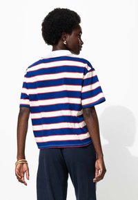 Polo rayé présentant des bandes bleues, rouges et blanches. Manches courtes et col, fabriqué à partir d'un tissu doux. Design simple et coupe décontractée.