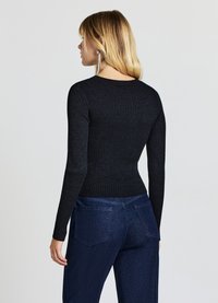 Schwarzes, geripptes Langarmshirt mit figurbetontem Schnitt, rundem Halsausschnitt und einer strukturierten Oberfläche, kombiniert mit dunkelblauen, hoch taillierten Jeans.