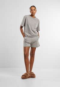 T-shirt gris à manches courtes avec une poche sur la poitrine, associé à un short gris assorti. Modèle portant des chaussons en fourrure marron. Texture lisse.