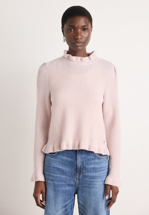 Light pink, ribbed knit sweater with a ruffled collar and hem. Long sleeves and relaxed fit. Paired with blue denim jeans.