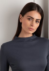 Maglione a maniche lunghe ribbed grigio scuro con colletto alto. Il tessuto appare liscio con una sottile texture e un motivo a righe uniforme.