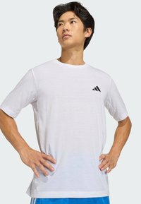 Camiseta blanca de manga corta hecha de una tela ligera con dobladillo curvado, que presenta un logo negro de Adidas en la parte superior izquierda.
