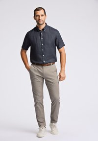 Camicia a maniche corte blu navy con bottoni, pantaloni grigi e sneakers bianche; vestibilità casual con linee pulite e trame sottili. Cintura marrone in evidenza.