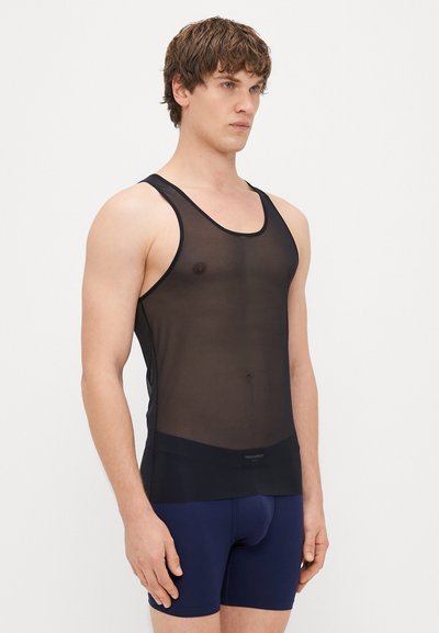 Fekete hálós ujjatlan felső kerek nyakkivágással és széles pántokkal, sima textúrával és testhezálló fazonnal, tengerészkék sort felett viselve.