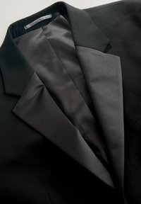 Sort blazer med satin revers, der viser en tekstureret yderside og en glat, skinnende indvendig foer. Har en struktureret krave og et skræddersyet design.