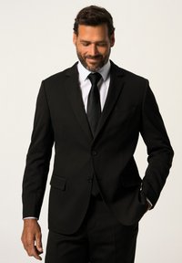 Abito nero con rever a punta, chiusura con un solo bottone e due tasche frontali. Abbinato a una camicia bianca e una cravatta nera. Tessuto liscio.