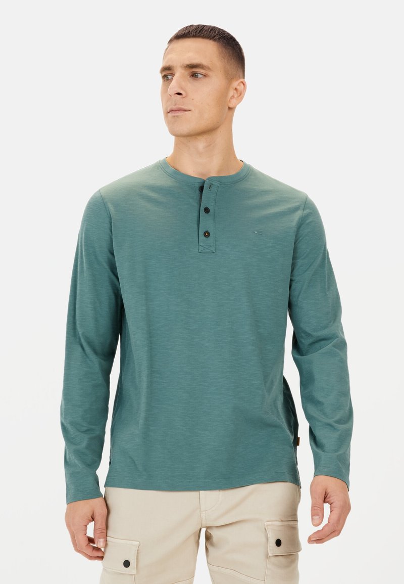 Langærmet teal henley skjorte med tre sorte knapper ved halsen, der har en glat overflade og lette sideslidser for komfort.