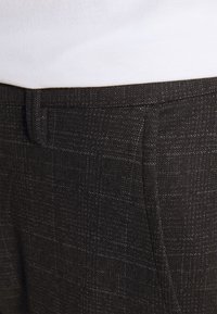 Ciemne spodnie w wzór w drobne kraty. Wykonane z teksturowanej tkaniny o subtelnej połysku, z elegancko wykończonymi kieszeniami.