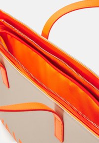 Beige handväska med orange interiör och handtag. Har två blixtlåsfack och två externa fickor med klara orange detaljer.