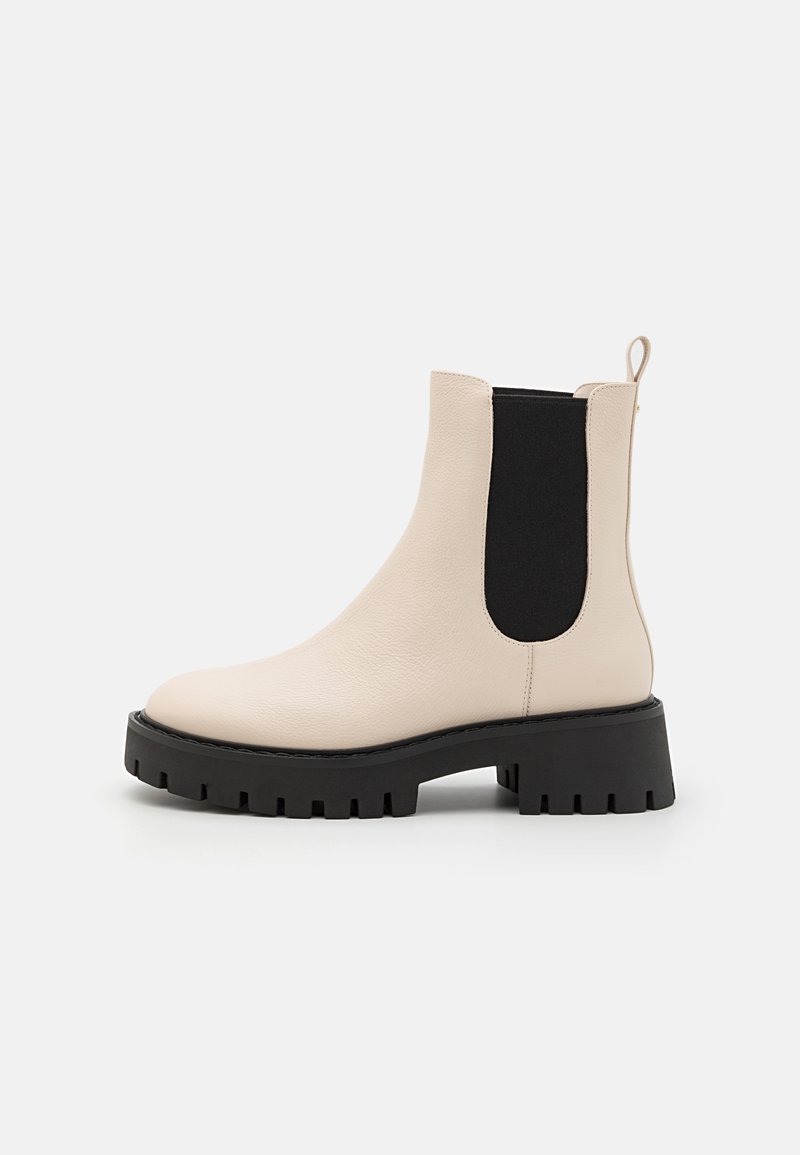 Bottine Chelsea en cuir beige avec panneau latéral élastique noir, semelle crantée noire épaisse, talon bloc et languette à l'arrière.