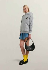 Molete cinzento com bolso frontal e gráfico de cartoon, saia pregueada azul, bolsa preta com detalhe de cartoon, meias amarelas, sapatos pretos.