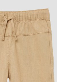 Beige geweven broek met een elastische tailleband en koord. Voorzien van een gladde textuur en contrasterende stiksels langs de naden.